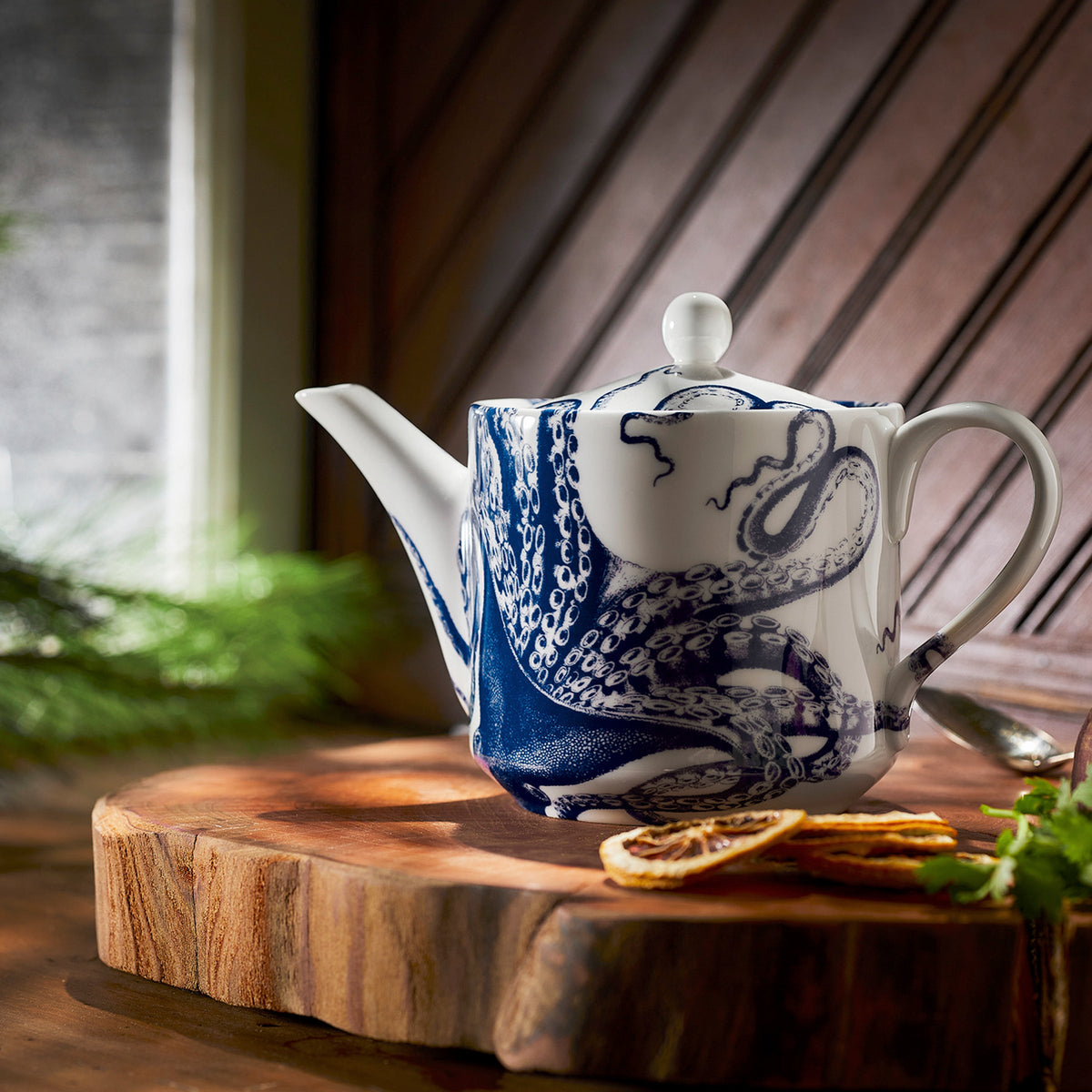 A Lucy Petite Teapot adorned with deepwater whimsy, resting on a wooden cutting board. (Brand Name: Caskata)