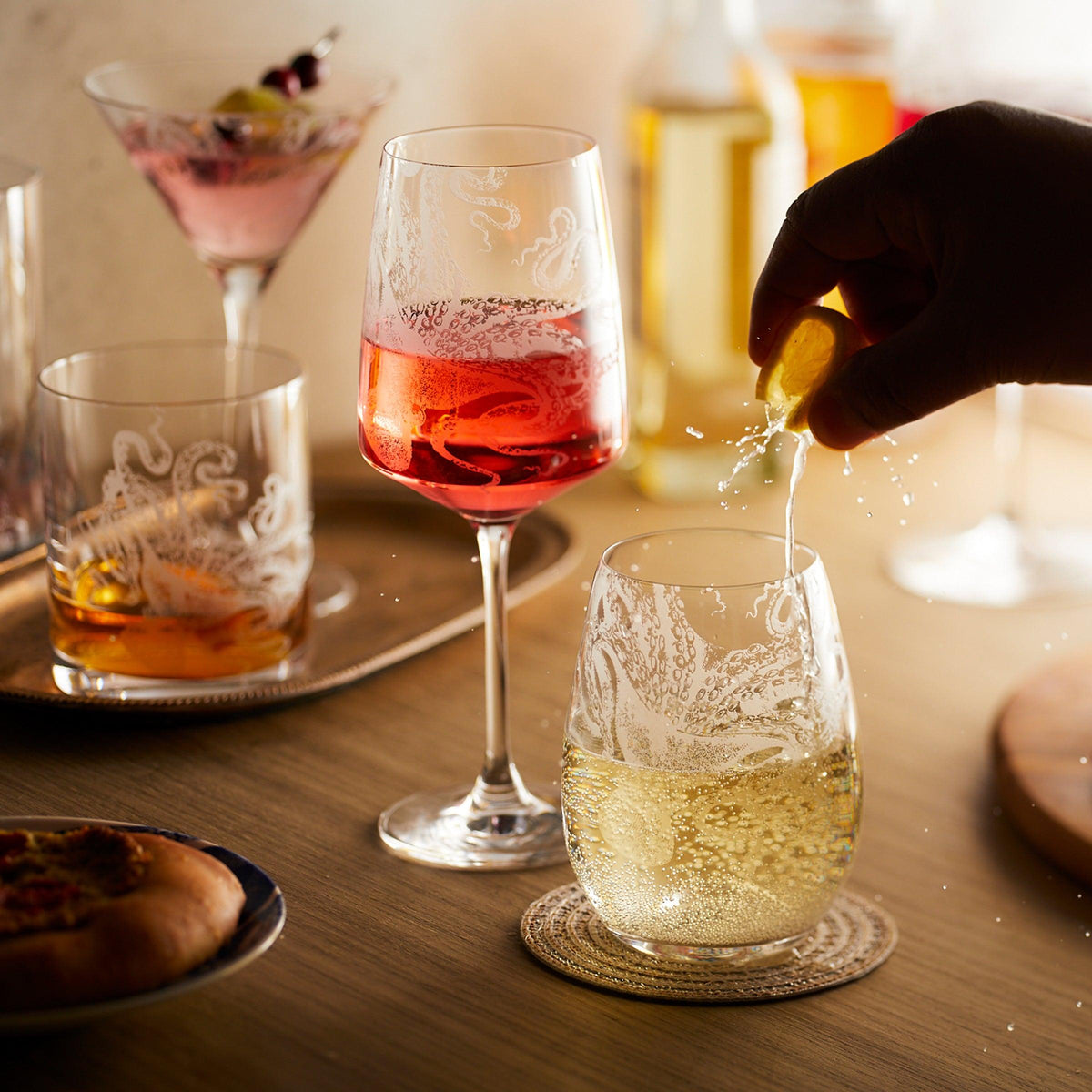 A collection of Lucy the octopus etched crystal glassware from Caskata, including red, white and stemless, filled with red and white wines.