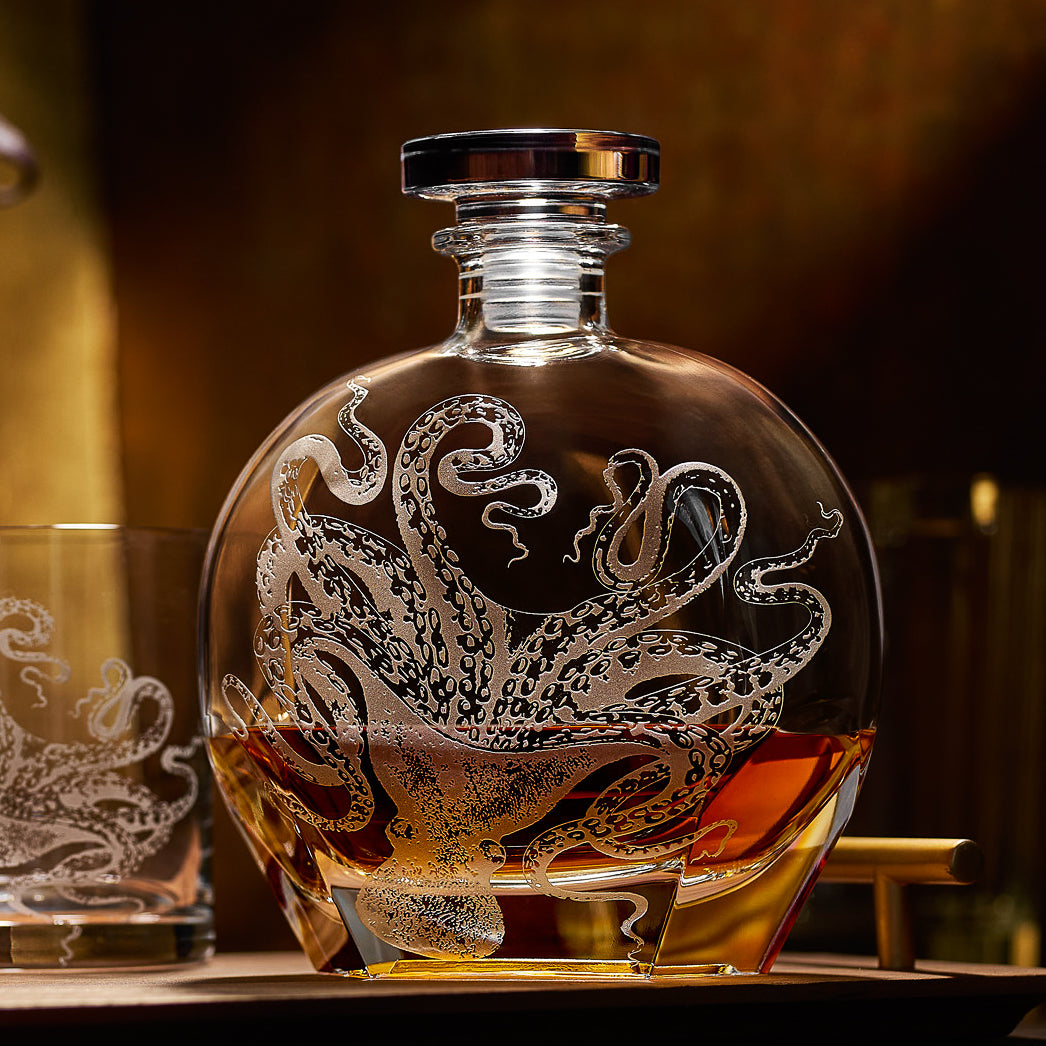 The "Lucy by the Fireside" Bundle by Caskata features a round octopus-etched decanter partly filled with amber liquid, paired with matching crystal rocks glasses—perfect for ocean-themed gifting.