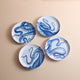 A set of four Lucy Melamine Small Plates by Caskata, featuring blue octopus designs, is displayed on a beige surface, highlighting their unbreakable style for any occasion.