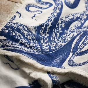 The Caskata Lucy Table Runner showcases a blue octopus tentacle print on white cotton with frayed edges—ideal for coastal table decor.