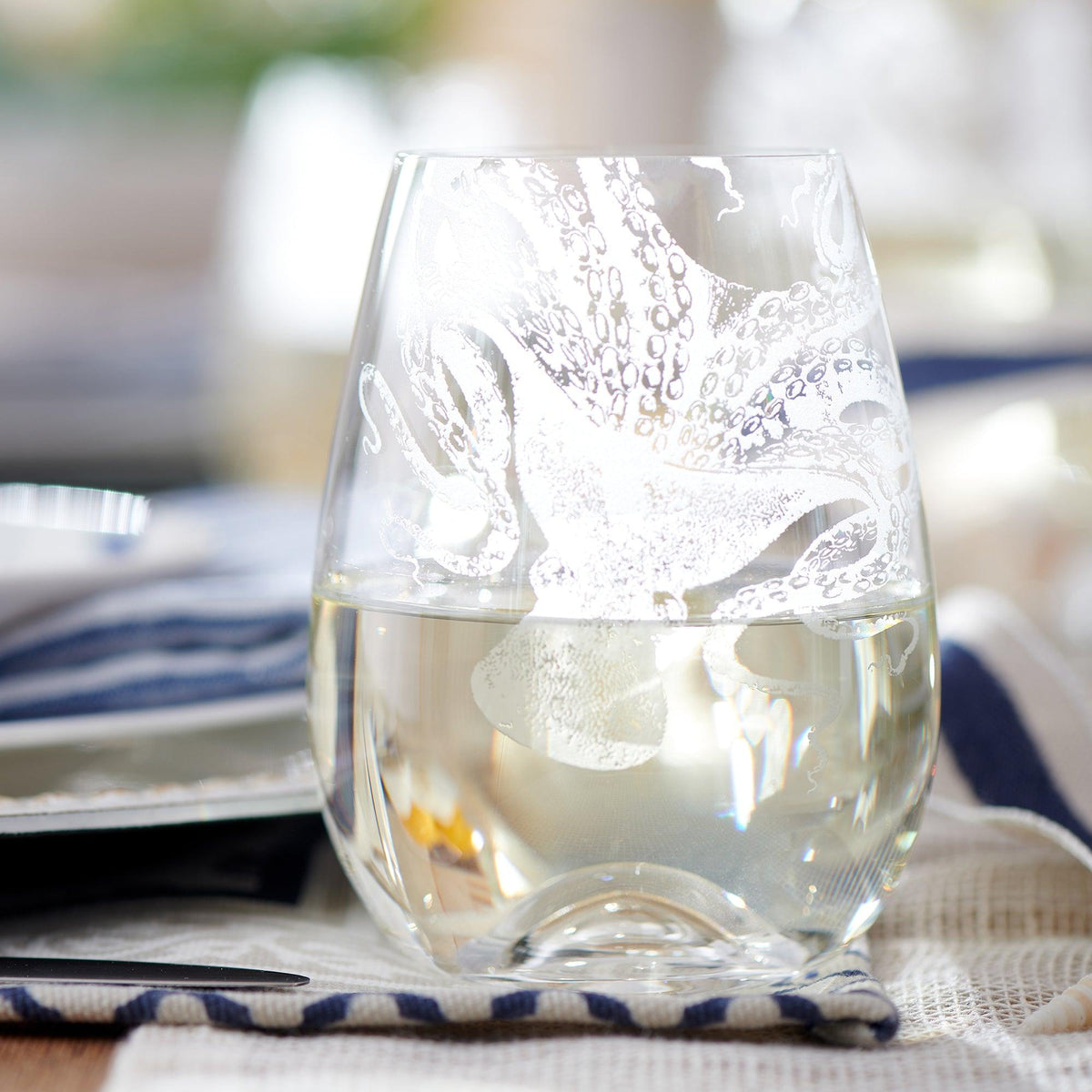 The "Lucy Al Fresco" Bundle by Caskata features a clear stemless wine glass with an etched octopus design, perfect for gifting or serving on a birchwood tray.