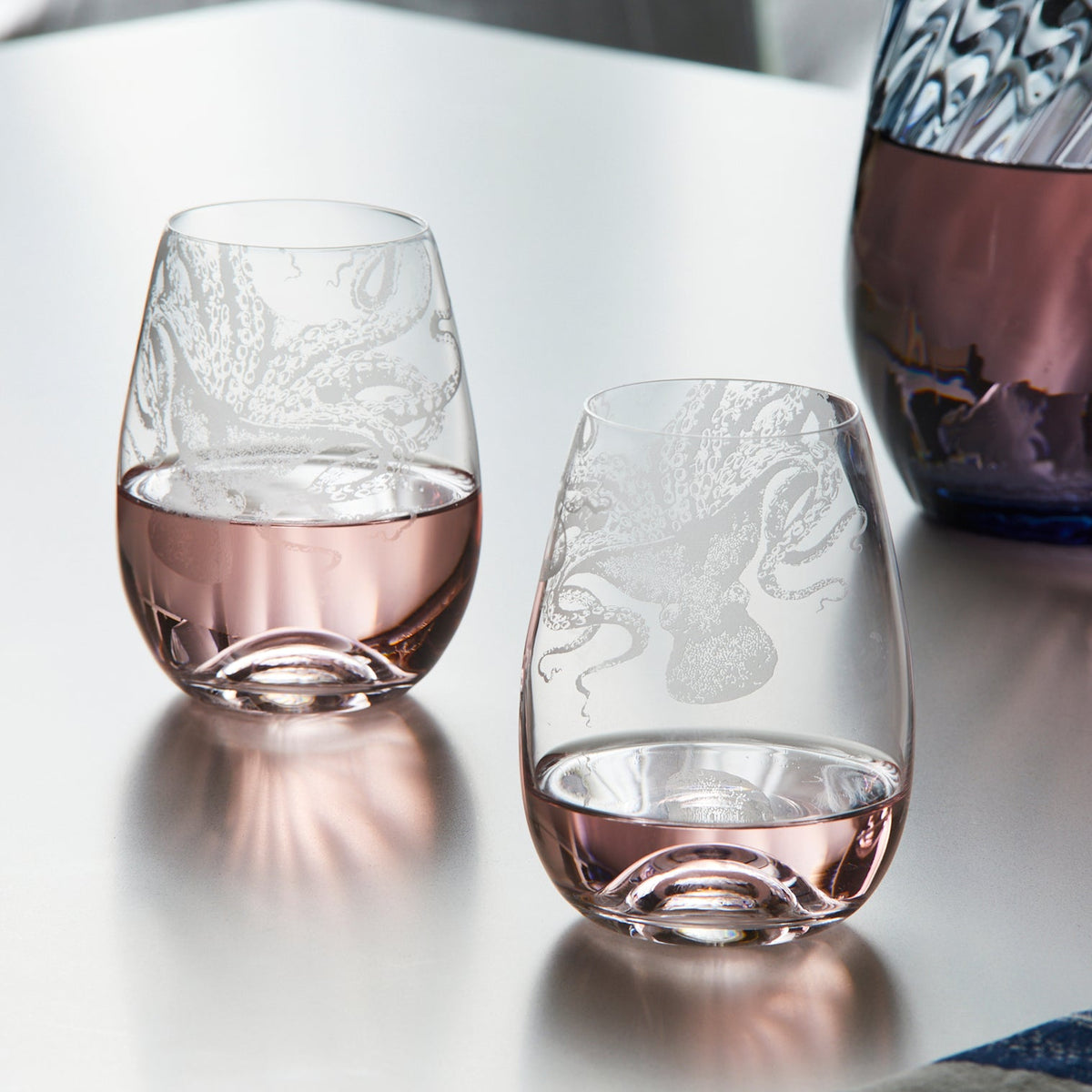 Two Lucy Stemless Wine Glasses by Caskata Artisanal Home on a table next to a vase.