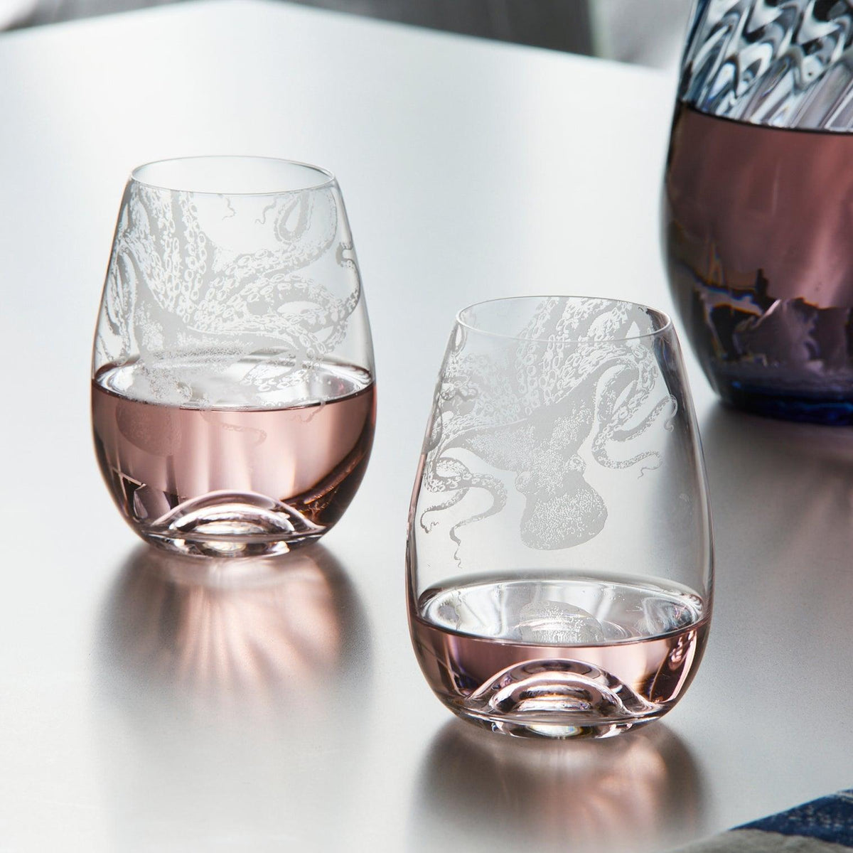 The "Lucy Al Fresco" Bundle by Caskata features two stemless wine glasses with etched octopus designs and a stunning blue and purple decanter—an ideal addition to any octopus-themed gift set.