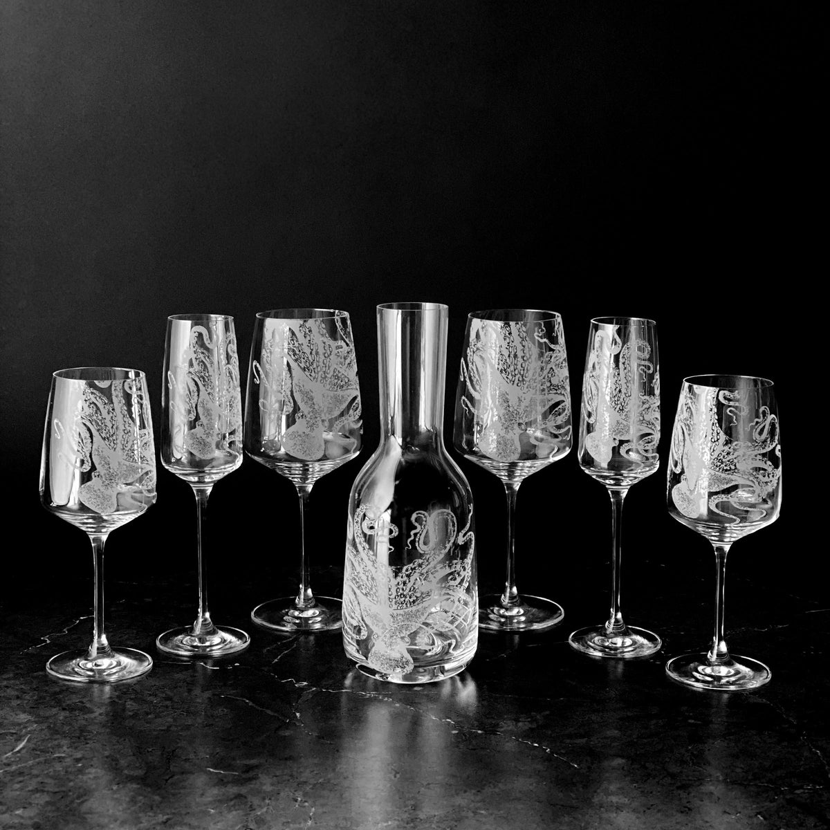 A black and white photo of a group of Lucy White Wine Glasses by Caskata Artisanal Home and a decanter.