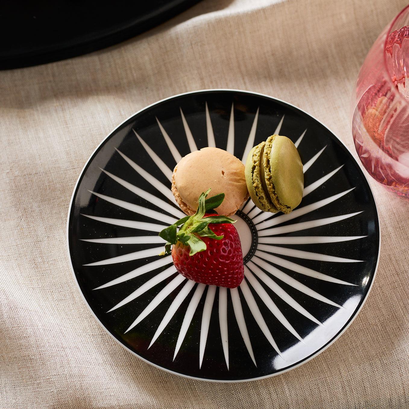 Four Marrakech Small Plates by Caskata Artisanal Home, each made of high-fired porcelain with white radial starburst patterns, are arranged in a staggered overlapping formation reminiscent of Marrakech's intricate designs.