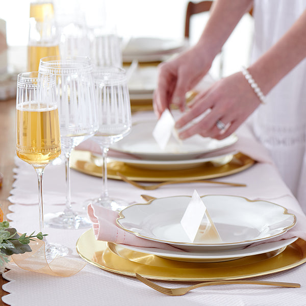 Hands Setting a Table for a Wedding with Champagne Glasses from the Marrakech Crystal Collection and Grace Gold Rimmed Dinner Plates from CASKATA