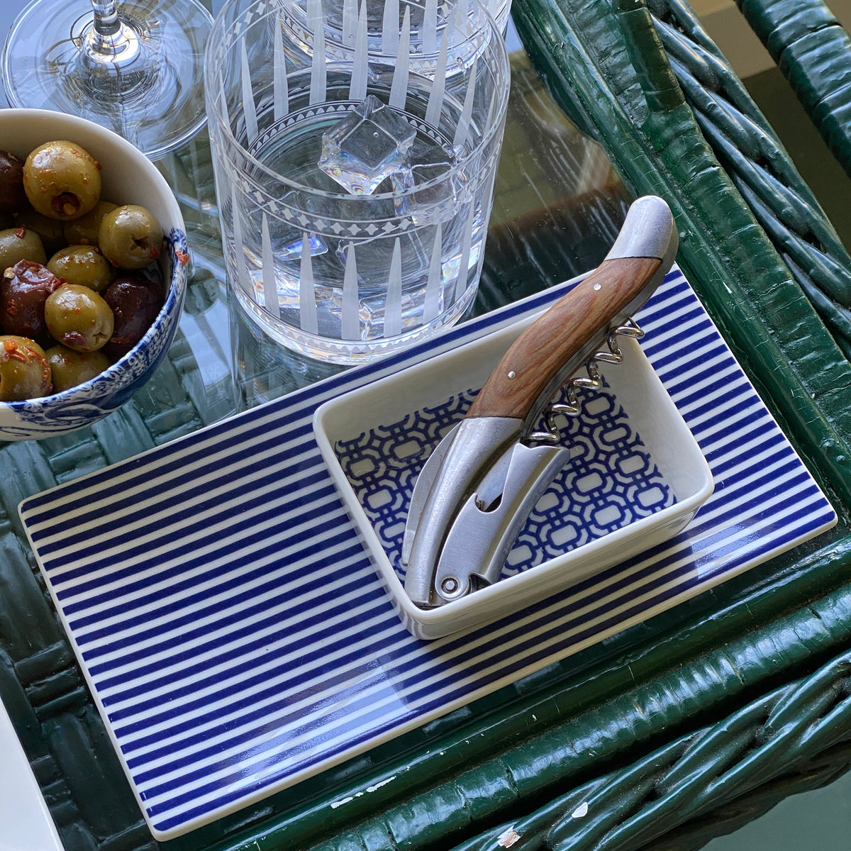 A blue and white striped Newport Nested Appetizer Tray &amp; Spoons Set with olives and a bottle of wine. (Brand: Caskata)