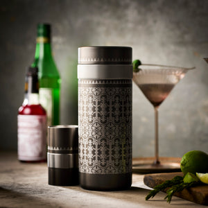 The Caskata Smoky Quartz Bar Bundle is displayed on a table with a martini glass, bottles, lime, and herbs—ideal for mixing cocktails or elevating your bar setup.