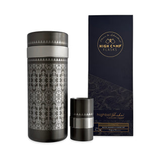 The Caskata x High Camp Casablanca Batch Cocktail Shaker with intricate patterns sits beside a matching jigger and a navy blue Caskata box featuring gold and silver branding.