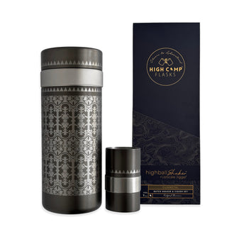 The Caskata x High Camp Casablanca Batch Cocktail Shaker with intricate patterns sits beside a matching jigger and a navy blue Caskata box featuring gold and silver branding.