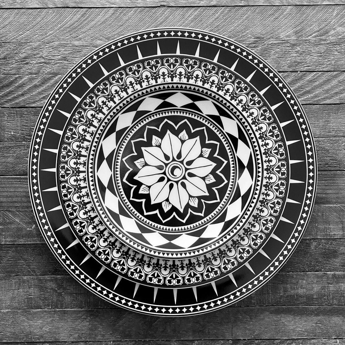 A black and white photo of the Marrakech Black Rimmed Dinner Plate with a flower design, found in the markets of Morocco, by Caskata Artisanal Home.