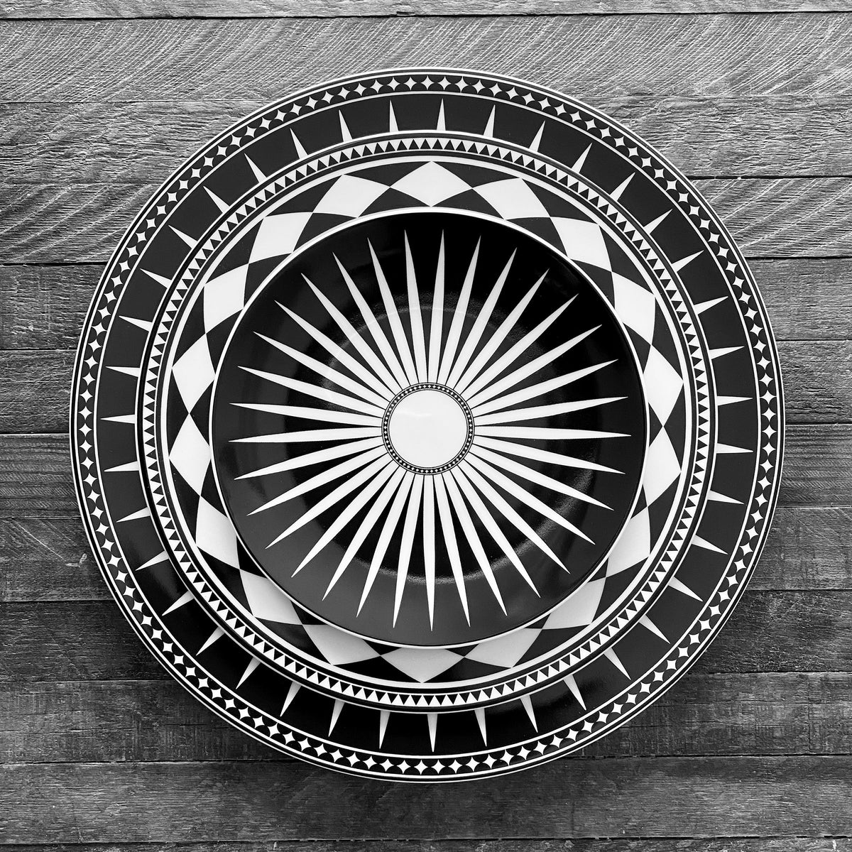 A black and white photo of a Marrakech Black Rimmed Dinner Plate with a geometric sunburst design, inspired by ceramics from Marrakech, created by Caskata Artisanal Home.