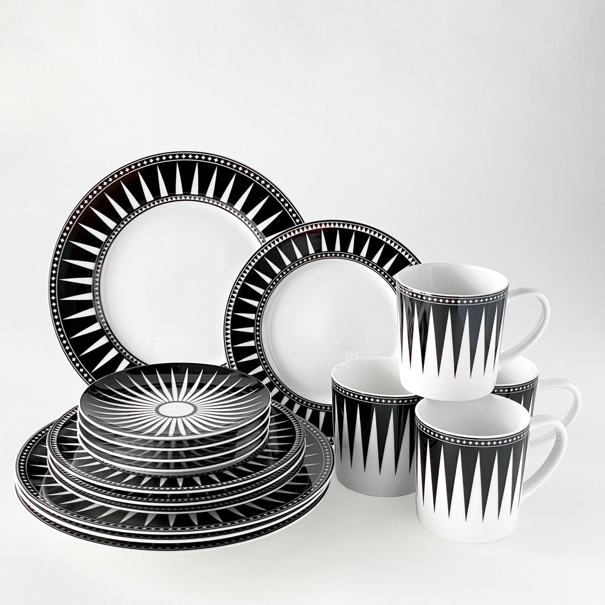 A black and white geometric patterned 16-piece dinnerware set in high-fired porcelain, including dinner plates, salad plates, bowls, and mugs, arranged on a white background. This exquisite Marrakech-inspired collection also features elegant Caskata Artisanal Home Marrakech Small Plates for a complete dining experience.