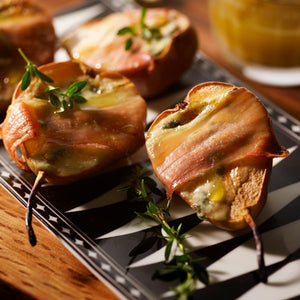 Pear halves grilled and wrapped in crispy bacon with melted cheese, garnished with herbs, presented elegantly on Caskata's Marrakech Petite Trays, Set of 2.