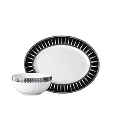 The Caskata Marrakech Serving Set features a white porcelain plate and bowl with black geometric rim patterns, inspired by Art Deco serveware, shown against a plain white background.