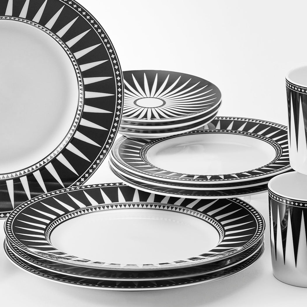 The Caskata Marrakech Table for 4 features a stunning set of black and white dinnerware beautifully arranged on a crisp white surface, creating an elegant table setting.