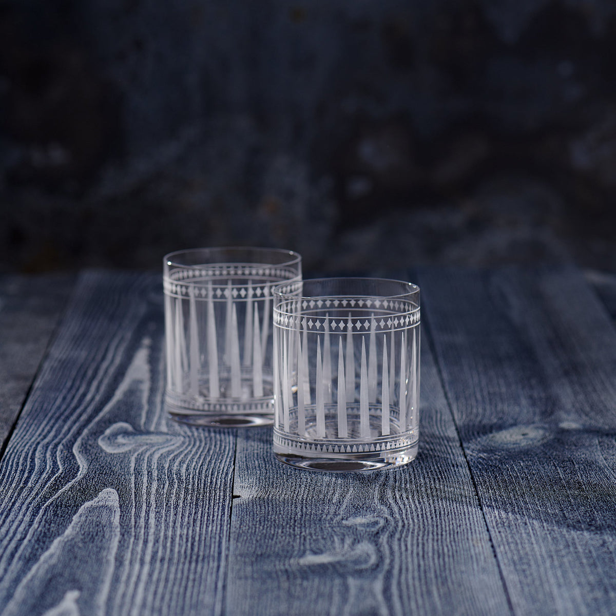 Two Marrakech Short Drink Glasses by Caskata Artisanal Home sitting on top of a wooden table in an Art Deco setting.