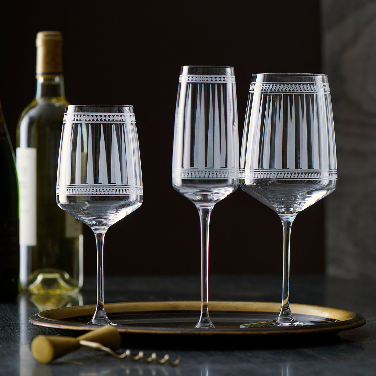 Three Marrakech White Wine Glasses by Caskata Artisanal Home on a tray next to a bottle of white wine.