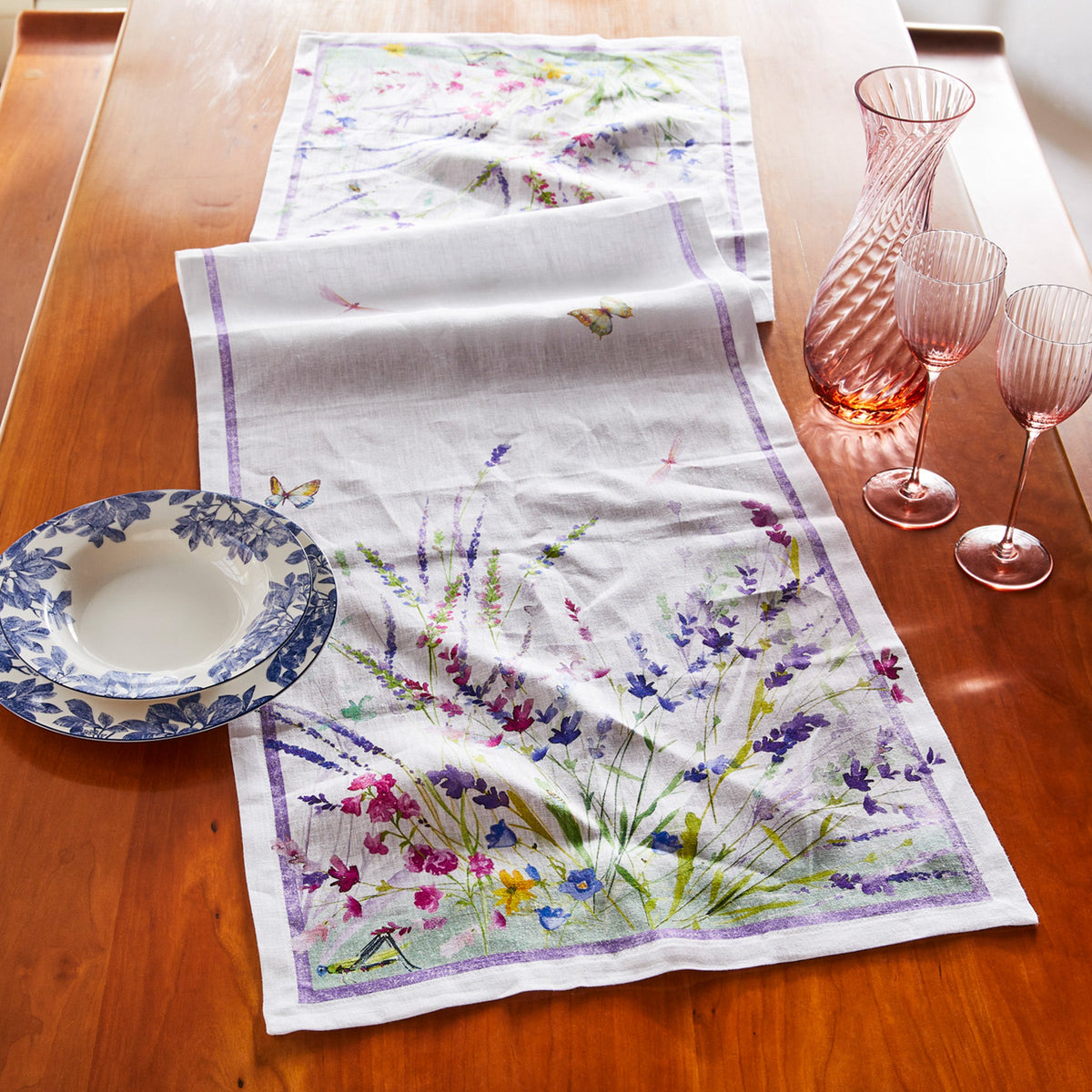 A Meadow Linen Table Runner adorned with wildflowers, hosting a plate and wine glasses by TTT.