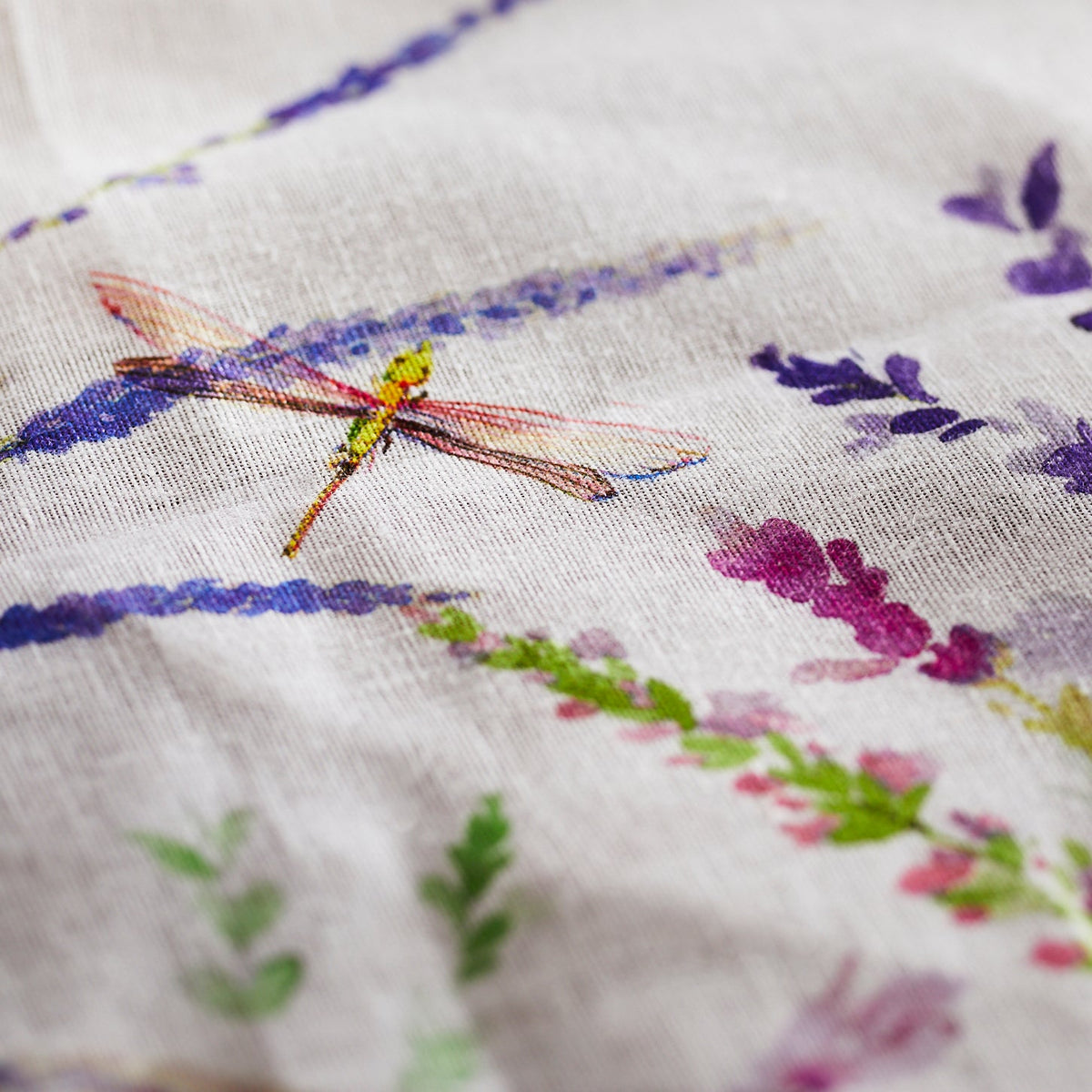 A dragonfly gracefully lands on a Meadow Linen Tablecloth adorned with delicate wildflowers from the brand TTT.