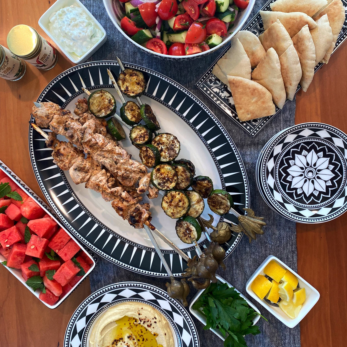 A Mediteranean feast is displayed on Caskata&#39;s black and white dinnerware. A large platter, canape plates, nested appetizer tray set, sushi trays an a large bowl hold kabobs, breads and salads.