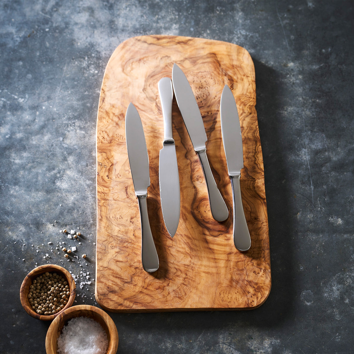 Four Mepra Mirror Set/4 Steak Knives on a wooden cutting board, polished to perfection.