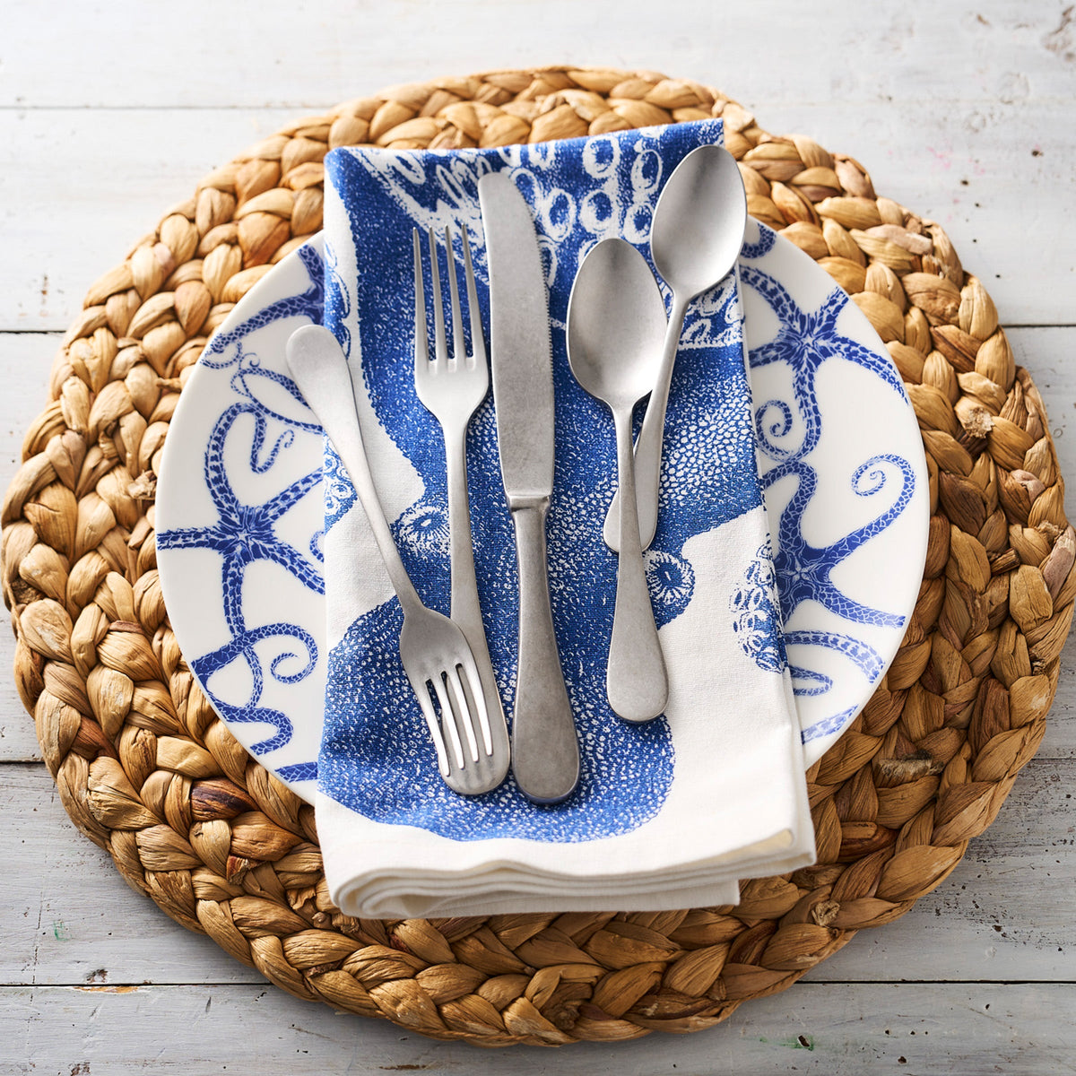 A timeless blue and white plate adorned with a Pewter 5-Piece Flatware Setting from the Mepra Pewter Collection.
