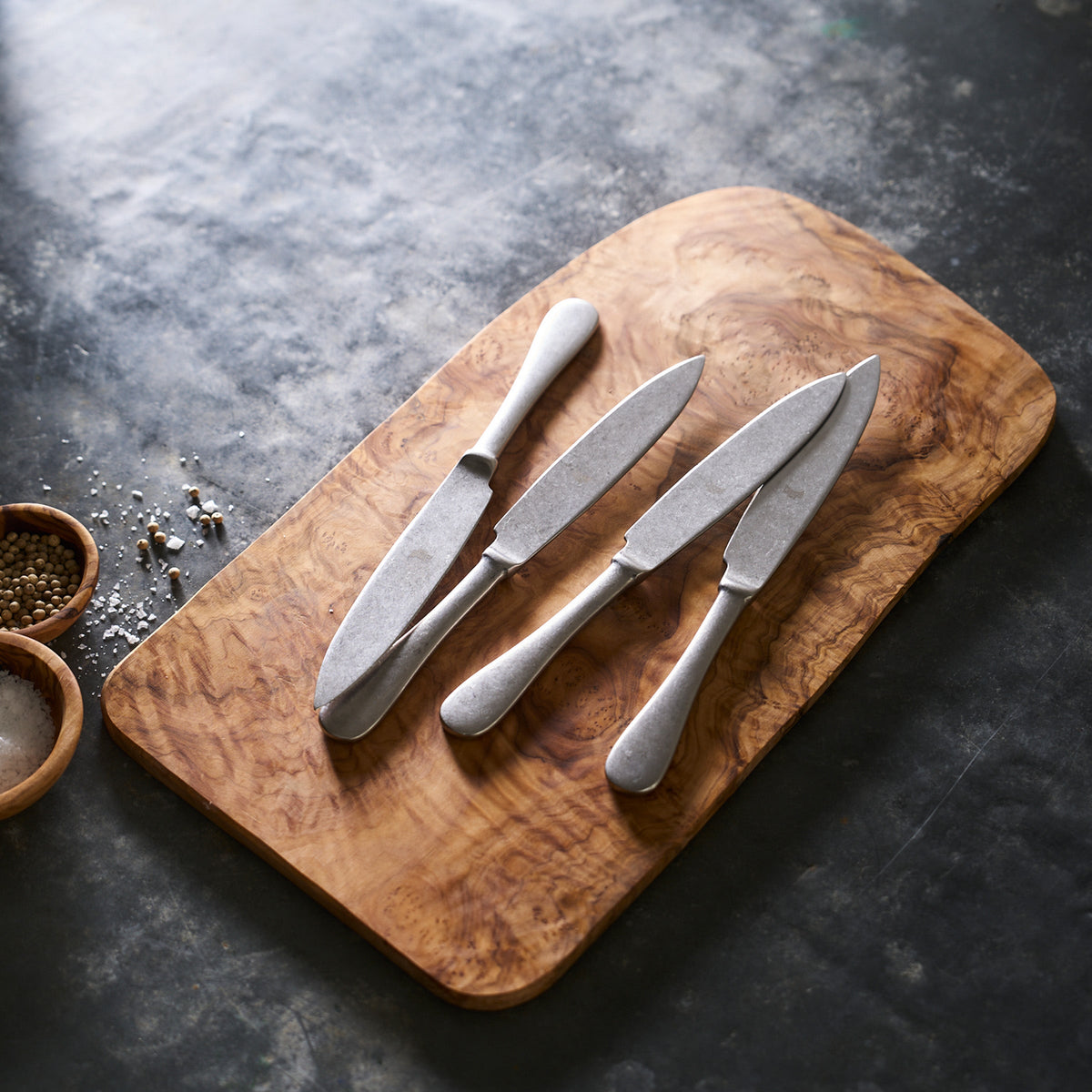Four Mepra Pewter Set/4 Steak Knives with a stonewashed finish on a wooden cutting board.
