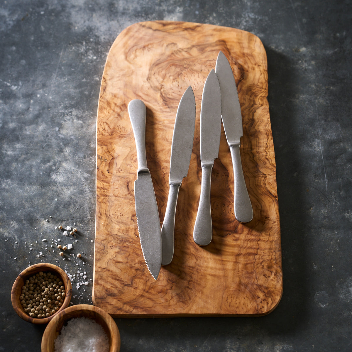 Four Mepra Pewter Set/4 Steak Knives with a stonewashed finish on a wooden cutting board.