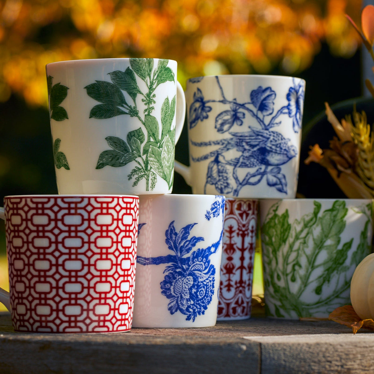 Caskata Artisanal Home&#39;s collection of Freya mugs with green floral designs sitting on a wooden table.