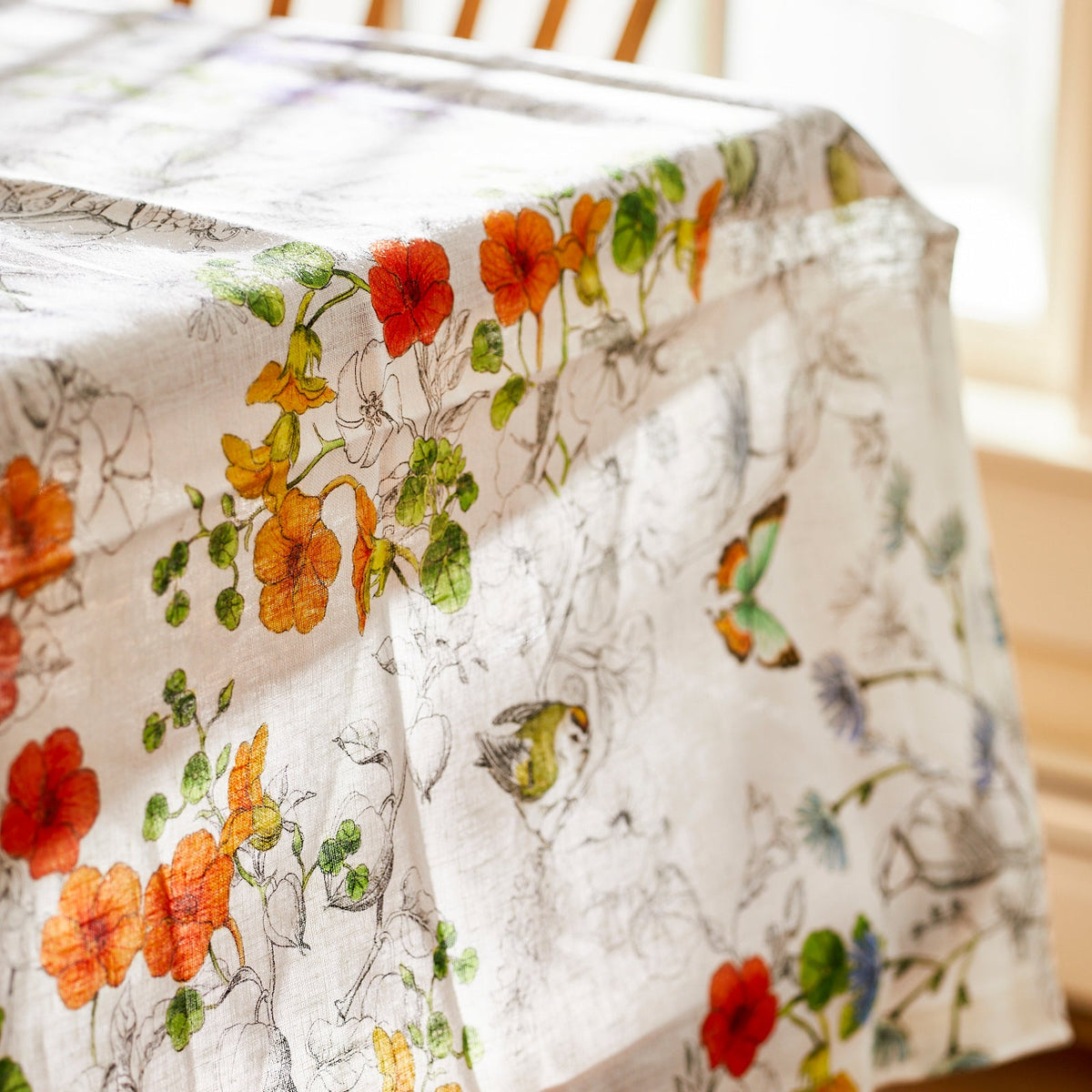 A Nasturtium linen tablecloth adorned with delicate flowers and graceful butterflies, expertly crafted by TTT, an Italian mill.
