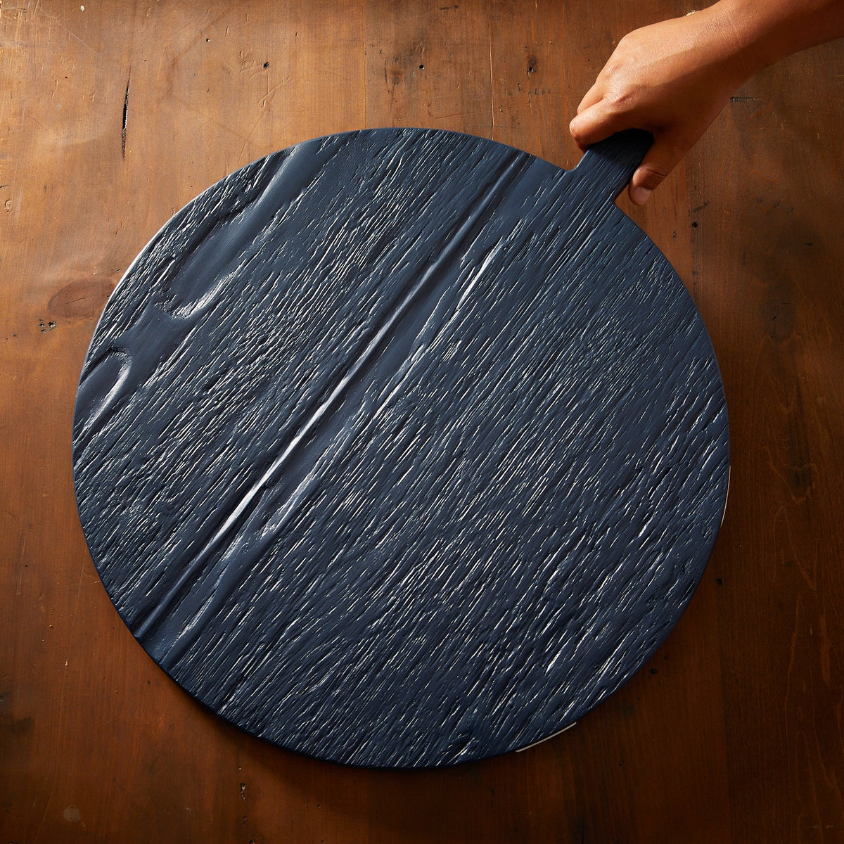 A person holding a Navy and White Round Charcuterie Big Board by Etu Home on a wooden table.