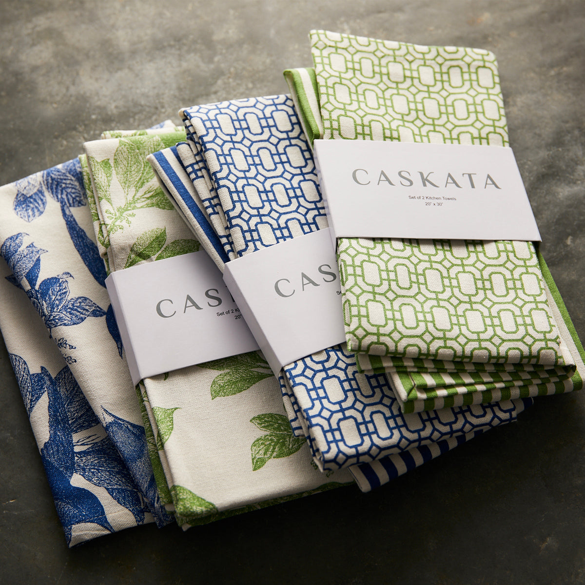 Three sets of Newport Garden Gate &amp; Pinstripe Verde Kitchen Towels, Mixed Set of 2, with Caskata labels, featuring blue, green, and white patterns reminiscent of Newport Garden Gate designs, are arranged on a dark textured surface. Perfect kitchen companions for any culinary setting.