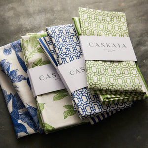 Three sets of Newport Garden Gate & Pinstripe Verde Kitchen Towels, Mixed Set of 2, with Caskata labels, featuring blue, green, and white patterns reminiscent of Newport Garden Gate designs, are arranged on a dark textured surface. Perfect kitchen companions for any culinary setting.