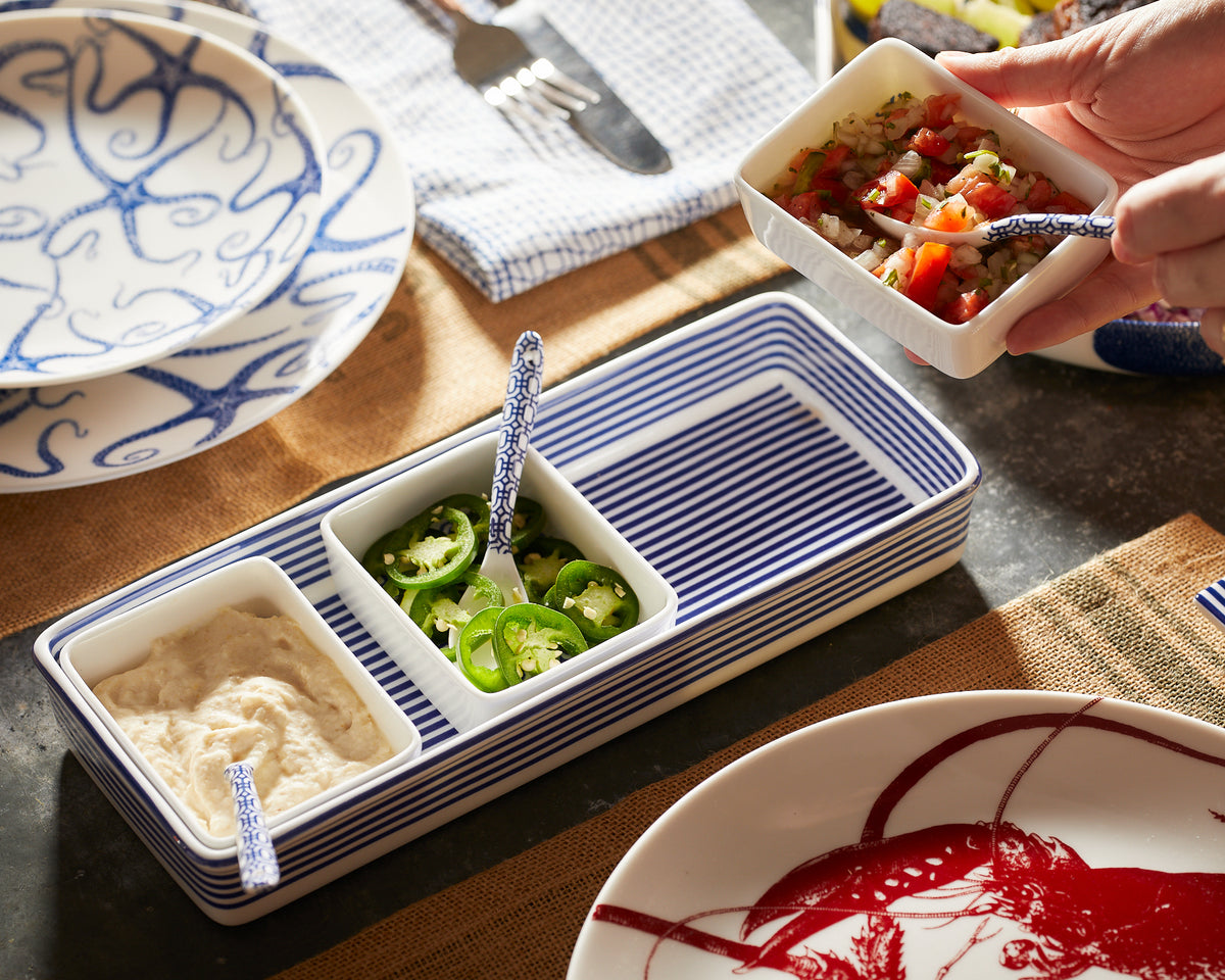 A person is holding a blue and white plate from a Caskata Newport Nested Appetizer Tray Set.