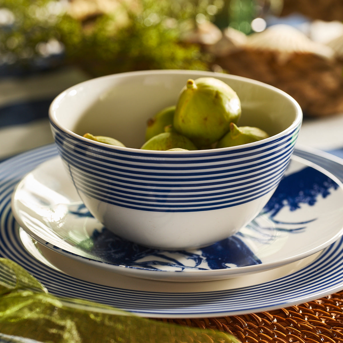 A Caskata Artisanal Home Newport Stripe Cereal Bowl with blue stripes, filled with green figs, rests on a matching blue and white plate atop a table.