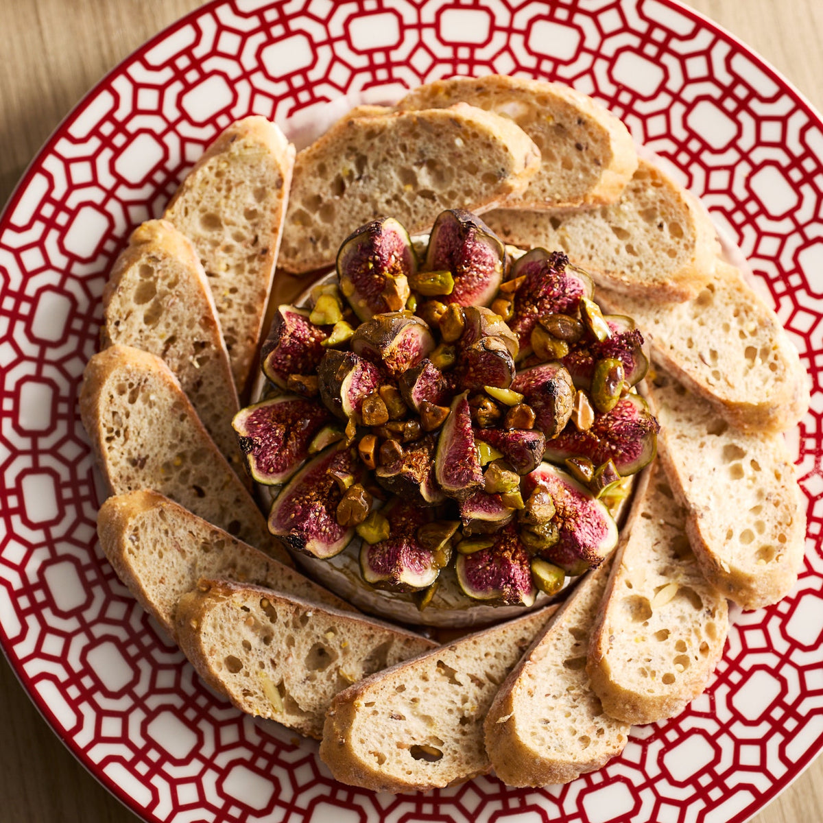 The Newport Crimson Garden Gate Table for 4 by Caskata is set for entertaining, with a wheel of cheese topped with figs and pistachios surrounded by baguette slices, perfect to complement your dinnerware.