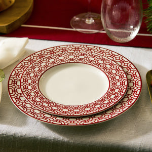 Two white plates from Caskata’s Newport Crimson Garden Gate Table for 4, with a red geometric design, are stacked on a white tablecloth next to a wine glass and napkin—a stylish porcelain addition to your dining table.