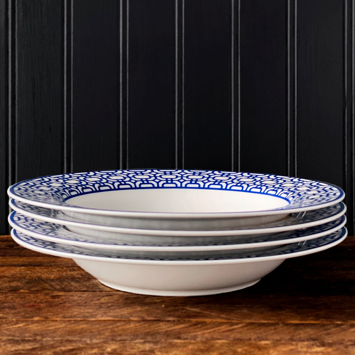 A set of Newport Garden Gate Rimmed Soup Bowls in blue and white, by Caskata Artisanal Home, on a wooden table.