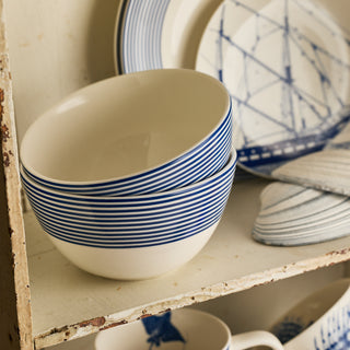 Two Caskata Artisanal Home Newport Stripe Cereal Bowls are stacked on a shelf beside plates with blue ship and stripe patterns.