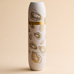 The Caskata x High Camp Crema Oysters Wine Flask by Caskata is a tall, white cylindrical flask featuring gold and brown oyster shell illustrations in a coastal motif, displayed upright against a beige background.
