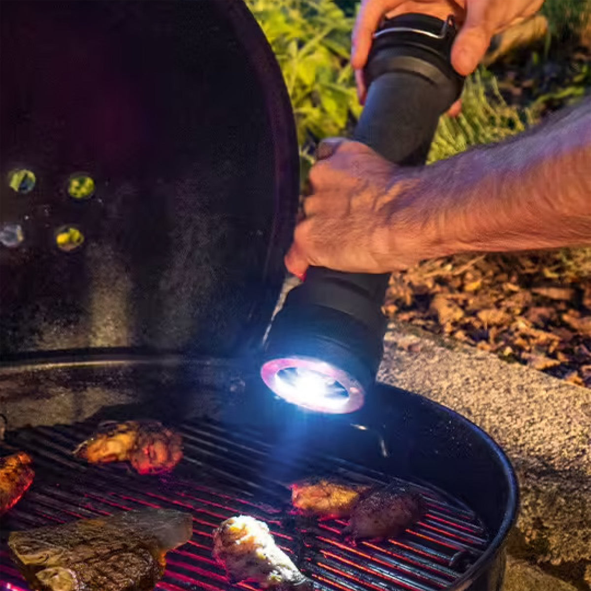 An individual is engaged in outdoor grilling, utilizing a LED light to navigate and a Peugeot BBQ 12&quot; Pepper Mill to season the food.