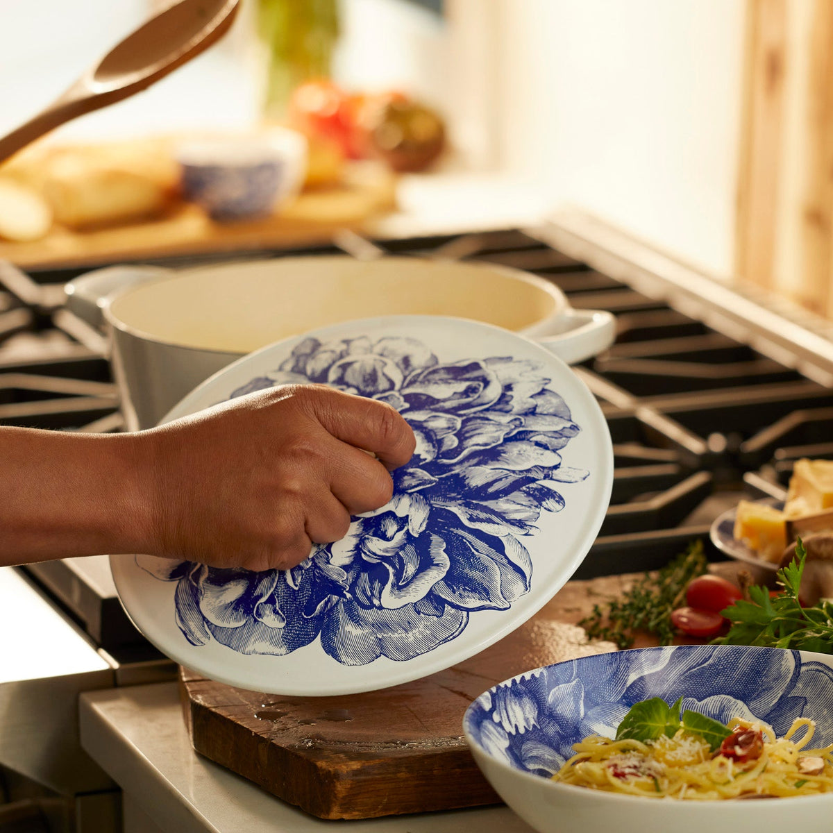 A person carefully placing a Caskata X Cuisinart Limited Edition Peony Enameled Cast Iron 5 Qt. Round Casserole with Lid on a stove for optimal heat retention.