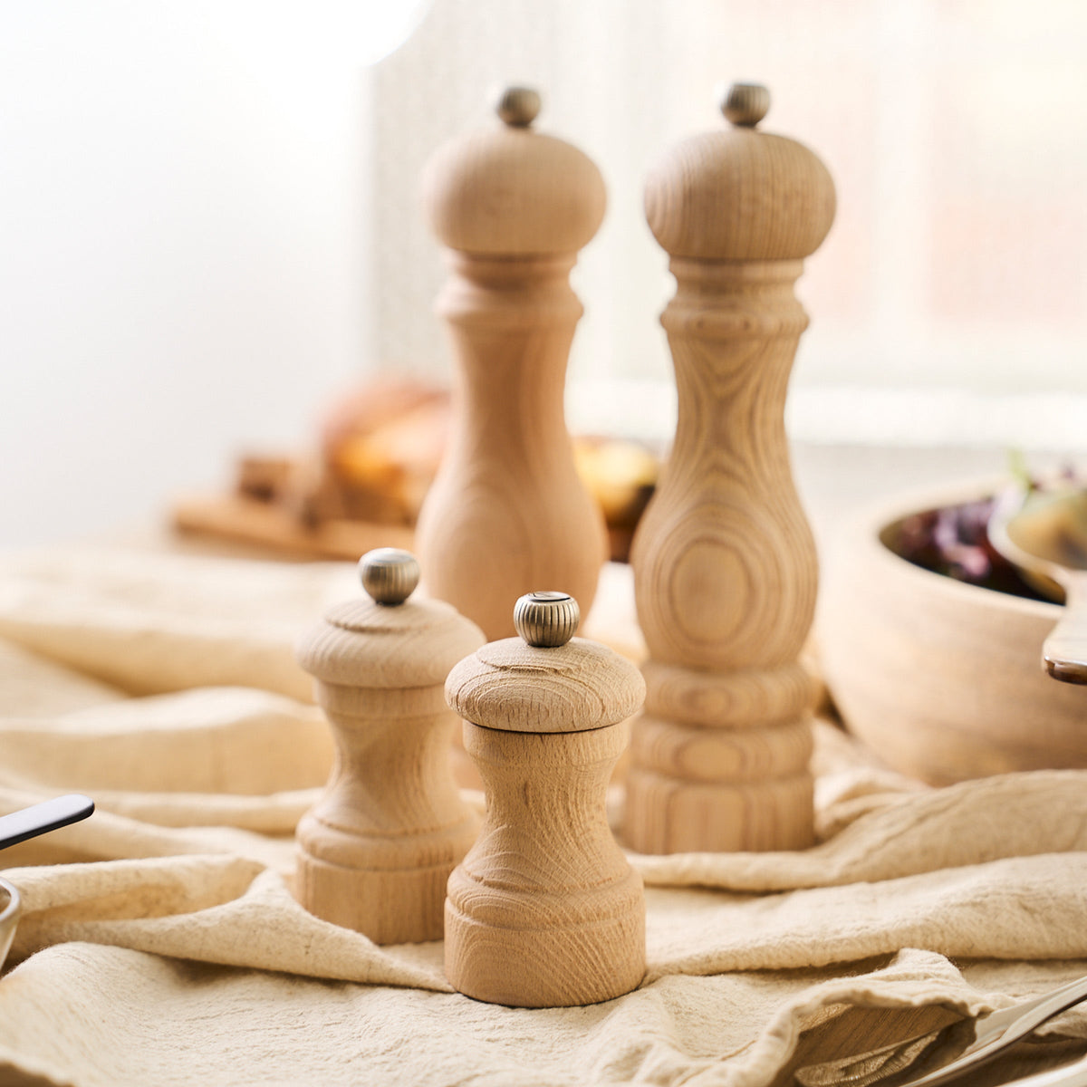 Three Peugeot Bistro 4&quot; Natural Salt &amp; Pepper Mills made of recycled beech wood on a table.