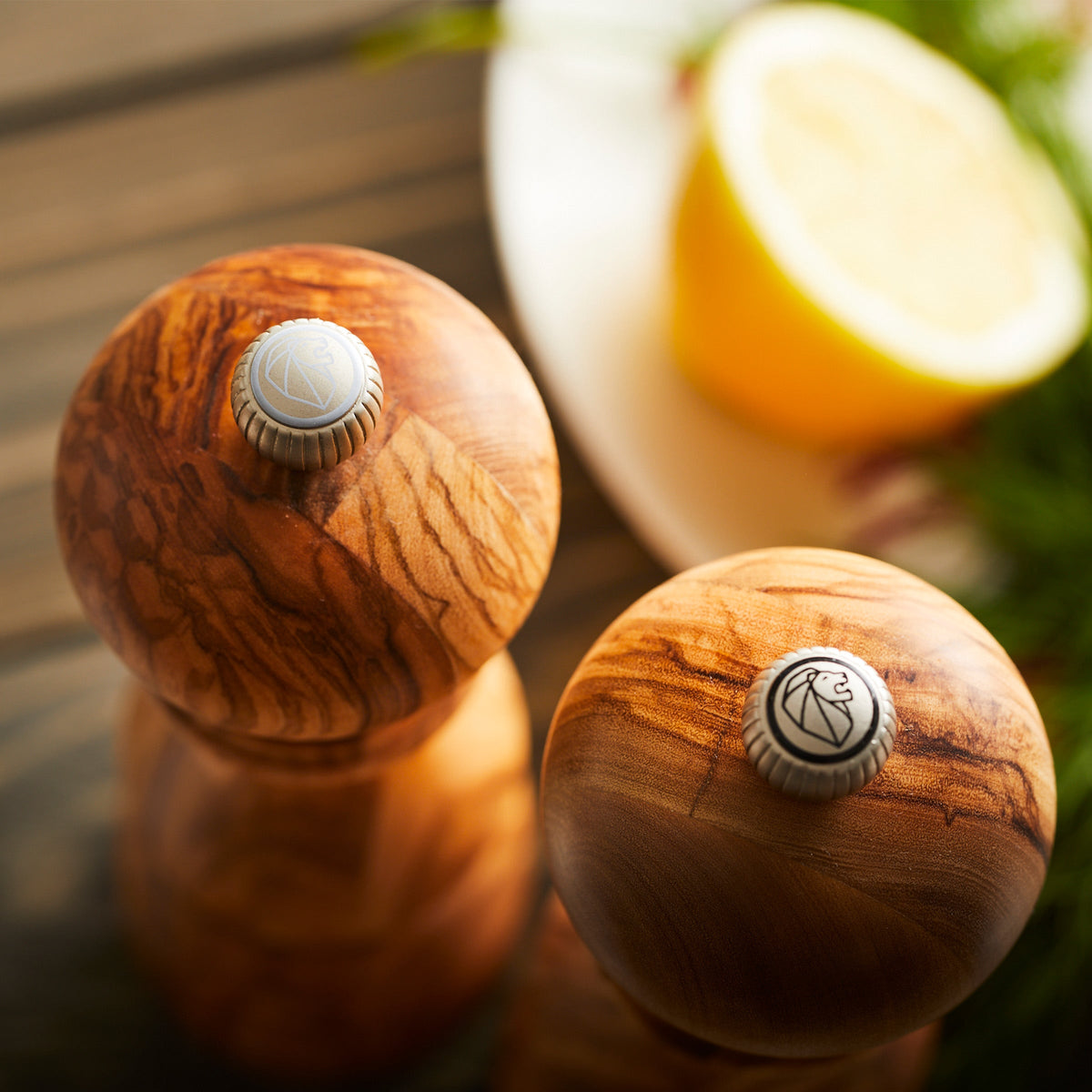 Two Paris 7&quot; Olive Wood Salt &amp; Pepper Mills from the renowned French brand Peugeot, featuring a classic silhouette, elegantly placed on a table.