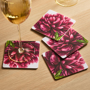 A wine glass sits elegantly on a Caskata Pink Peony Birchwood Coaster, set of 4, with FSC-certified trays scattered across the wooden table.