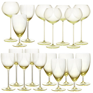 The Quinn Citrine Perfect Place Settings Set by Caskata features sixteen mouth-blown crystal wine glasses with light yellow-tinted stems and bowls, beautifully arranged in two rows against a white background.
