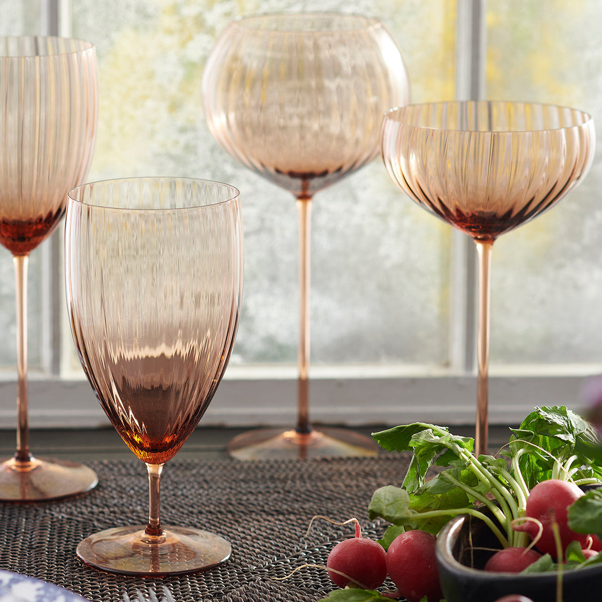 Quinn Amber Coupe Glasses Set/2 - Caskata Hand blown glassware in a window setting with radishes.