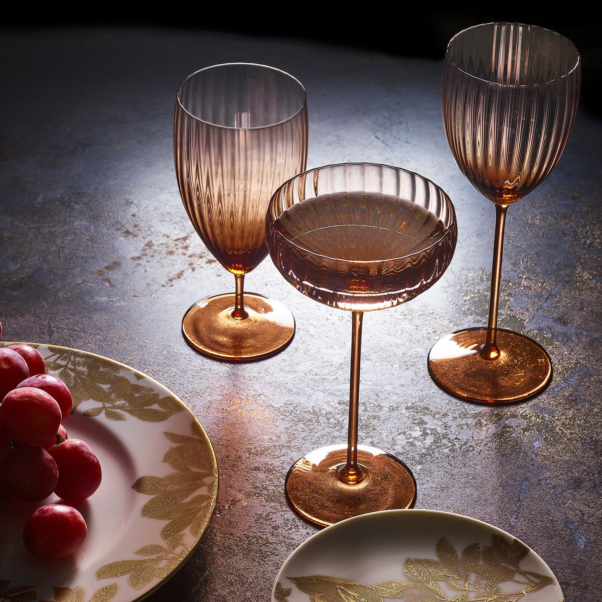 Quinn Amber Mouthblown Crystal Stemware from Caskata, featuring coupe, everyday and white wine shapes accompanied by gold Arbor dinnerware.